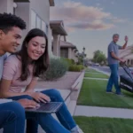 Couple looking at laptop on apartment steps in Queen Creek with man mowing lawn across street