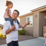 Father carrying daughter in front of new house in Buckeye Arizona at sunset