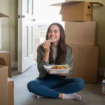 Woman eating takeout on floor of new Santa Ana apartment surrounded by moving boxes