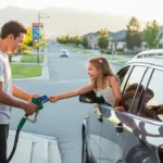 Father pumping gas with daughter's help at a West Jordan corner station at sunset.
