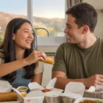 A young couple enjoys a takeout dinner together in their Irvine apartment kitchen at sunset.