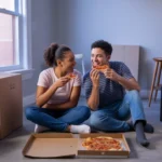 A couple eating pizza on the floor of their new apartment in Rock Hill, SC surrounded by moving boxes